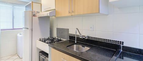 Cozinha compacta com fogão a gás, pia e armários de madeira.