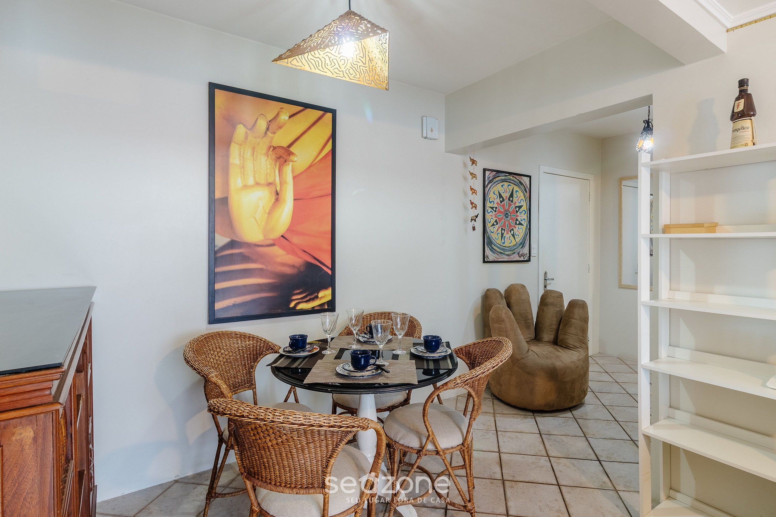 A dining area with wicker chairs, a round table, and a large painting on the wall.