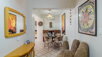 A dining area with a round table, wicker chairs, and a hanging light fixture.