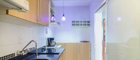 A modern kitchen with a black countertop, stainless steel sink, and wooden cabinets. There is a coffee maker on the counter and pendant lights above.