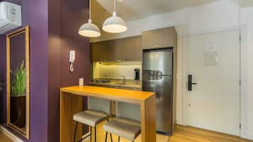 Cocina compacta con una mesa de madera y dos sillas, un refrigerador de acero inoxidable y una lámpara colgante.