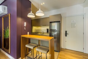 Cocina compacta con una mesa de madera y dos sillas, un refrigerador de acero inoxidable y una lámpara colgante.