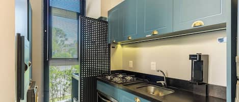 A compact kitchen with a gas stove, a sink, and a window with blinds.
