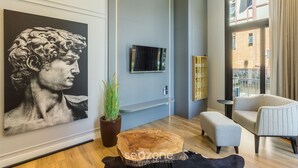 A modern living room with a large black and white painting, a flat-screen TV, a potted plant, a wooden coffee table, a grey sofa, and a black leather ottoman. - Elegant apt in the Heart of Gramado Cbg0106 (Gramado)