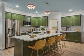 Une cuisine moderne avec des meubles de couleur verte, des appareils en acier inoxydable et un îlot central doté de tabourets de bar.