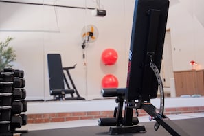 Un gimnasio con equipo de ejercicios, un ventilador de pared y pelotas de ejercicio rojas.