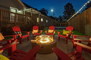 Un patio trasero con un brasero rodeado de sillas Adirondack rojas.