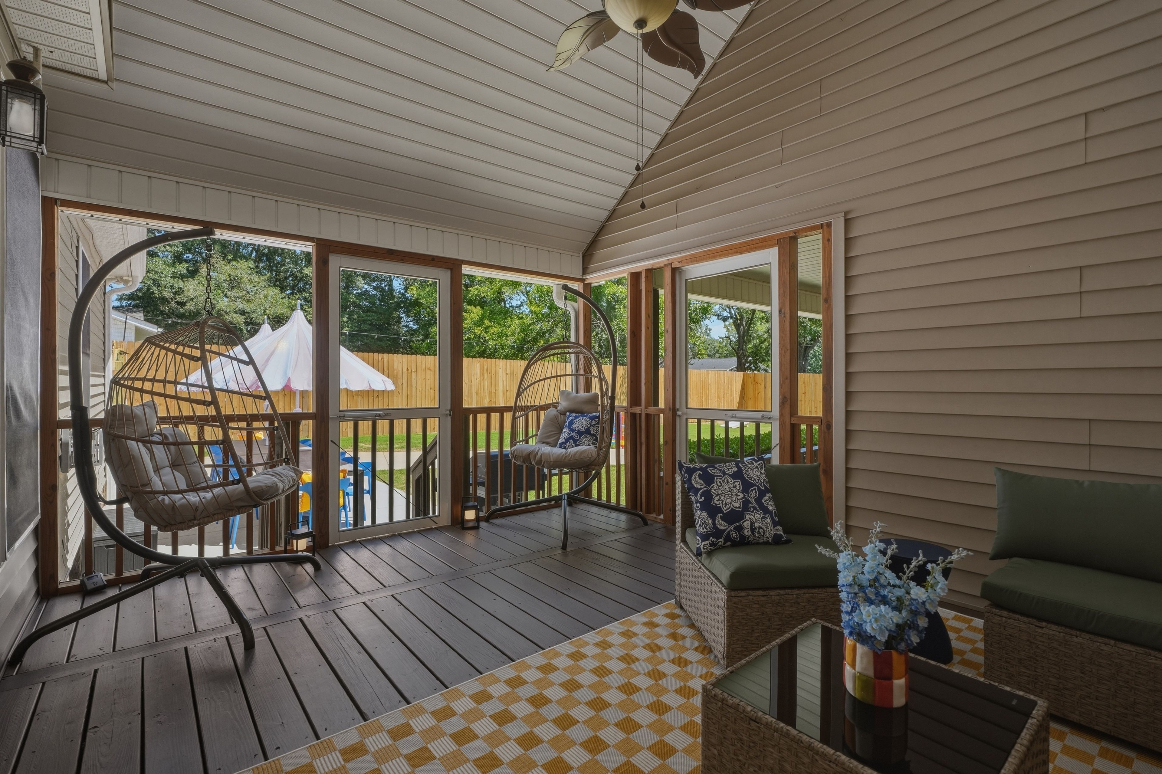 A covered outdoor deck with wicker furniture, a checkered mat, and a potted plant.