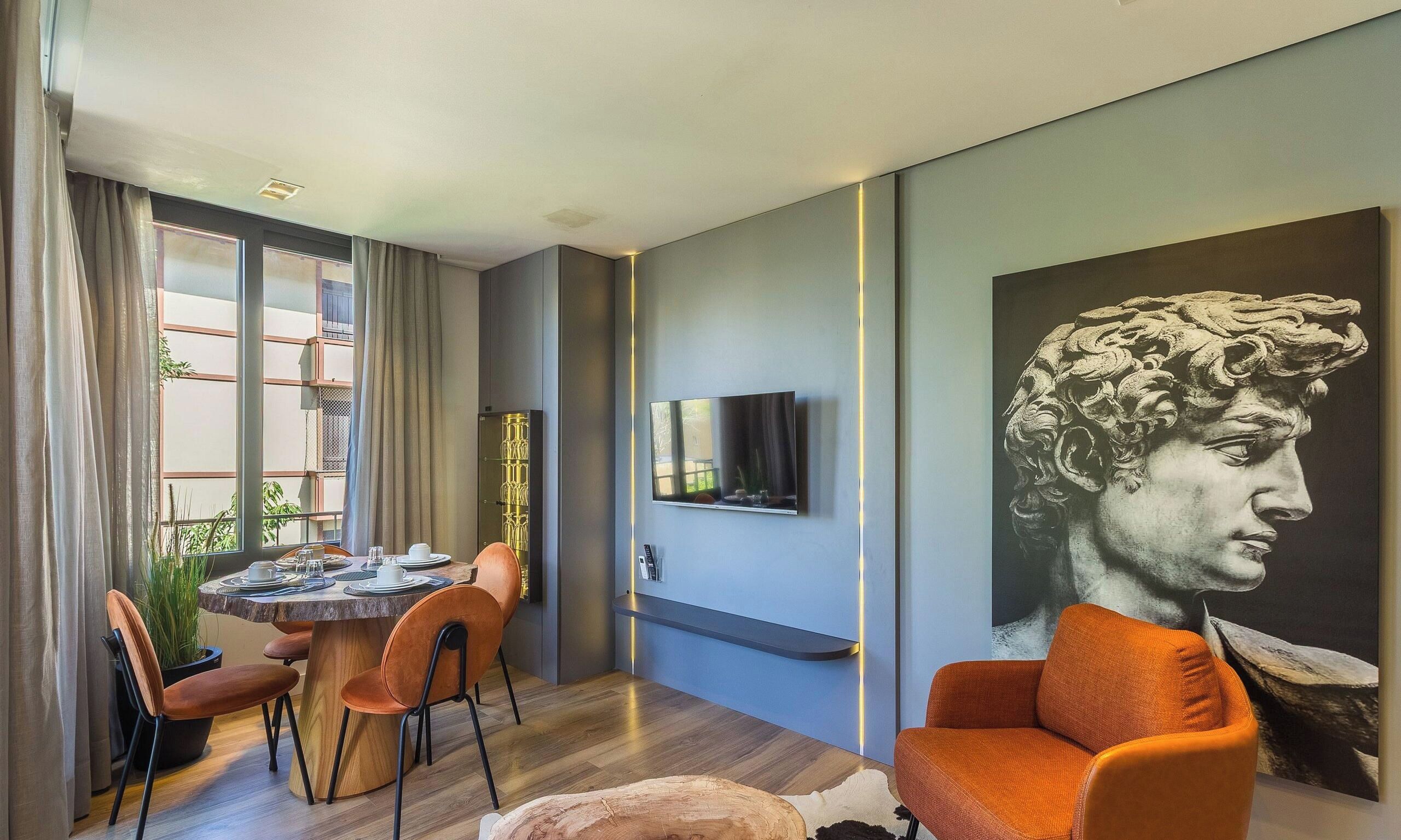 A modern living room with a dining area, a flat-screen TV mounted on the wall, and a large artwork.