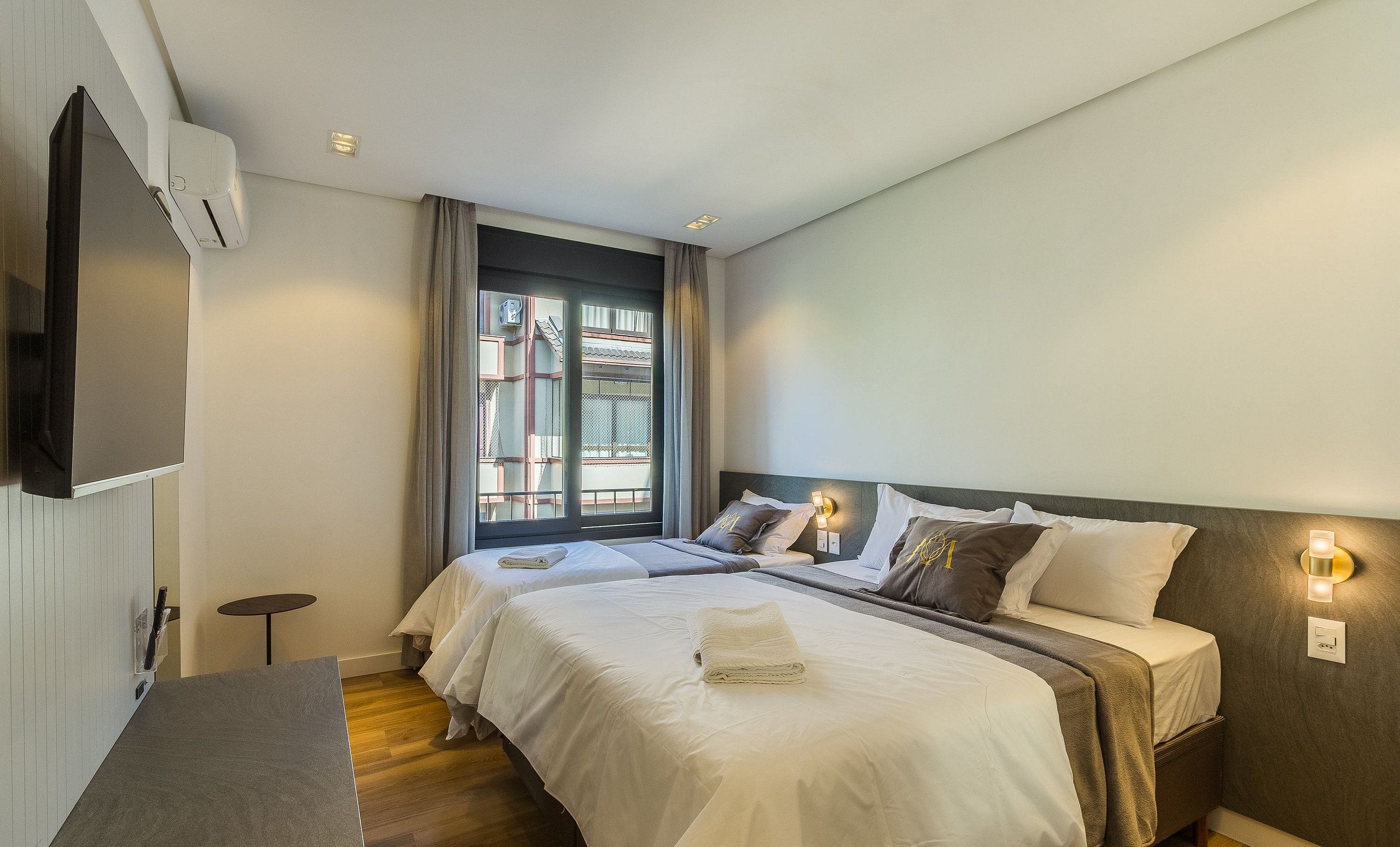 A hotel room with two beds, a TV, a window with curtains, and a bedside table.