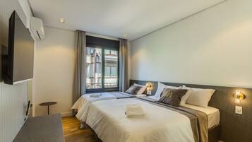 A hotel room with two beds, a TV, a window with curtains, and a bedside table.