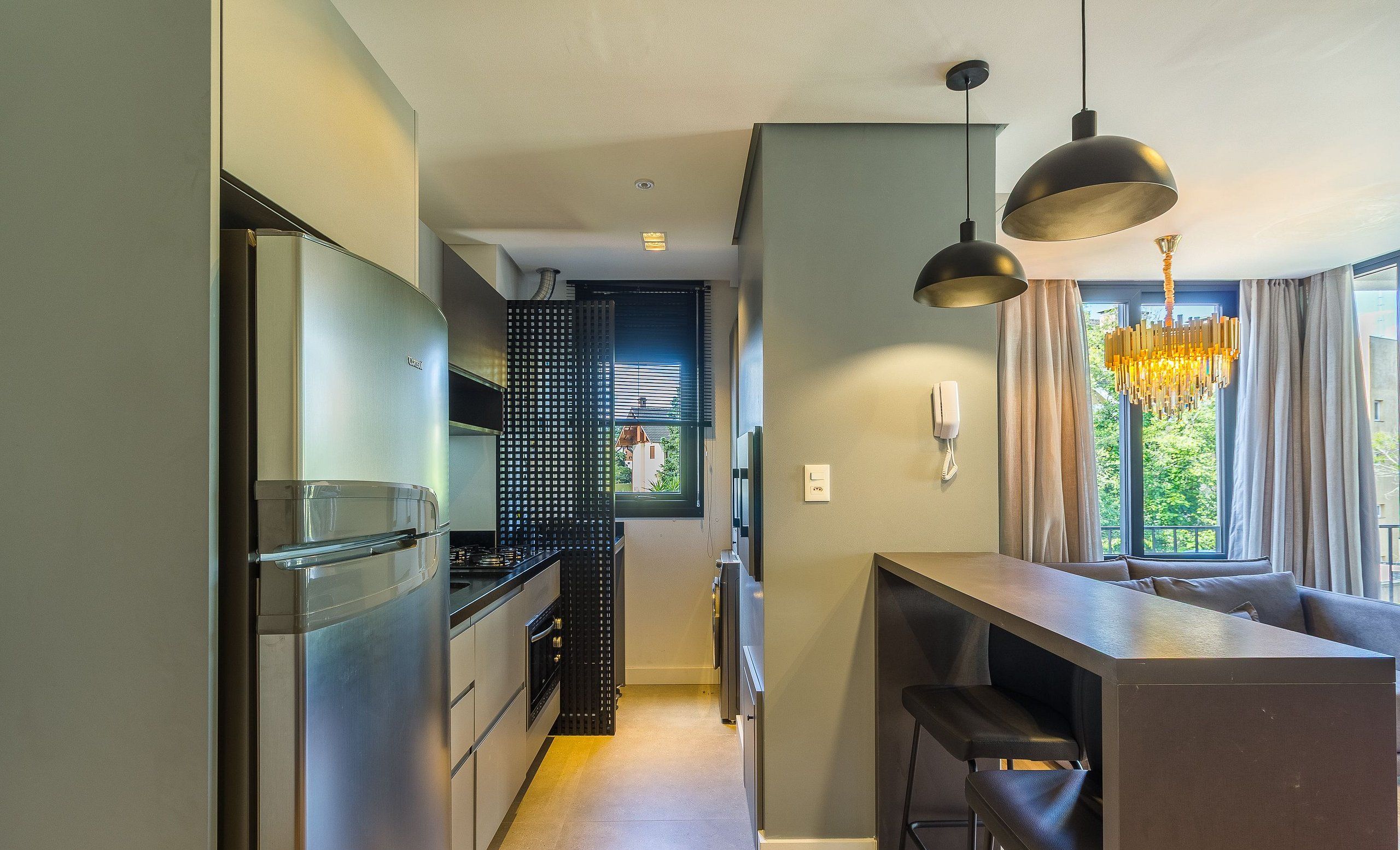 Una cocina moderna con electrodomésticos de acero inoxidable, un comedor con un taburete de bar y una ventana con vistas a zonas verdes.