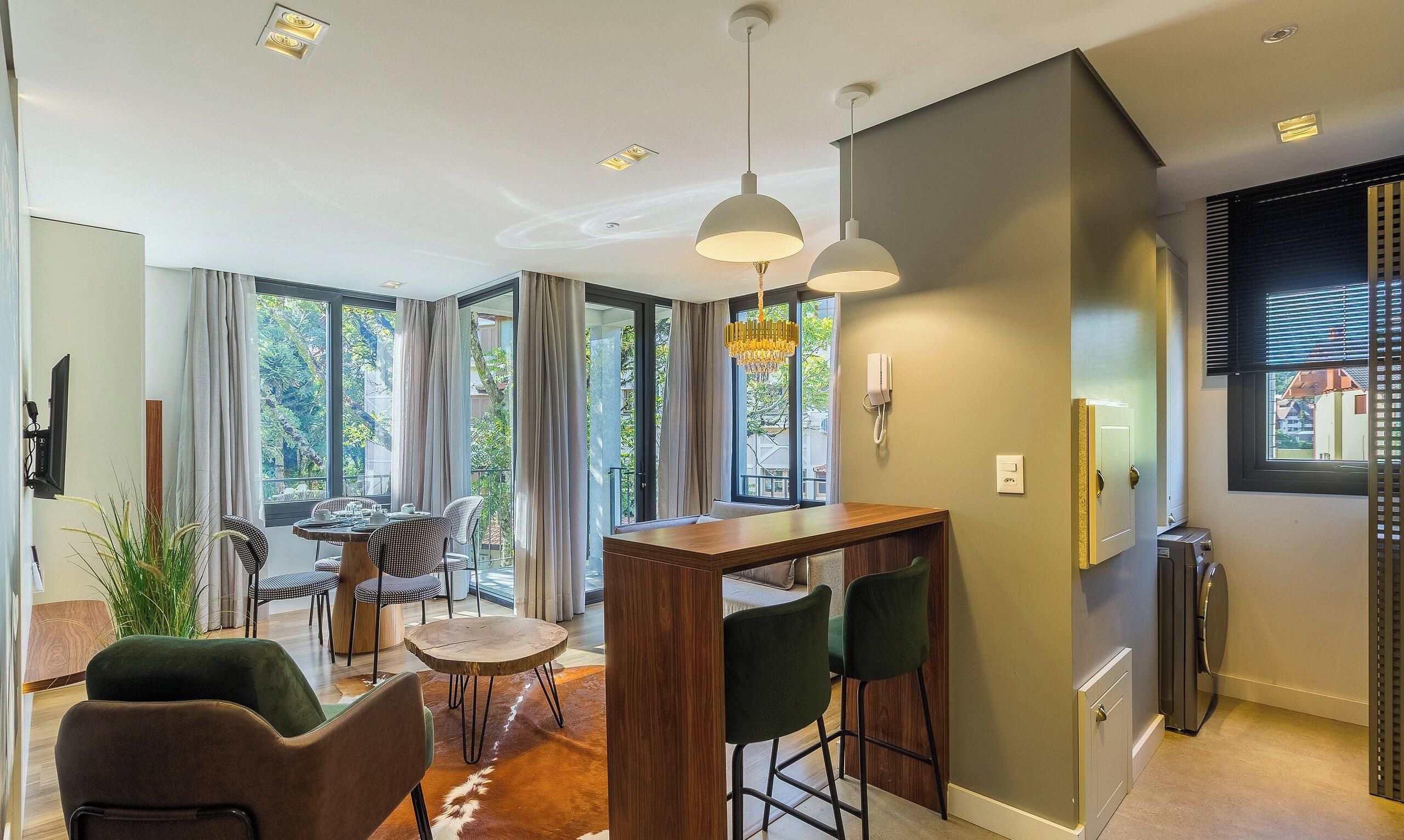 A modern kitchen with a dining area, large windows, and a view of greenery.