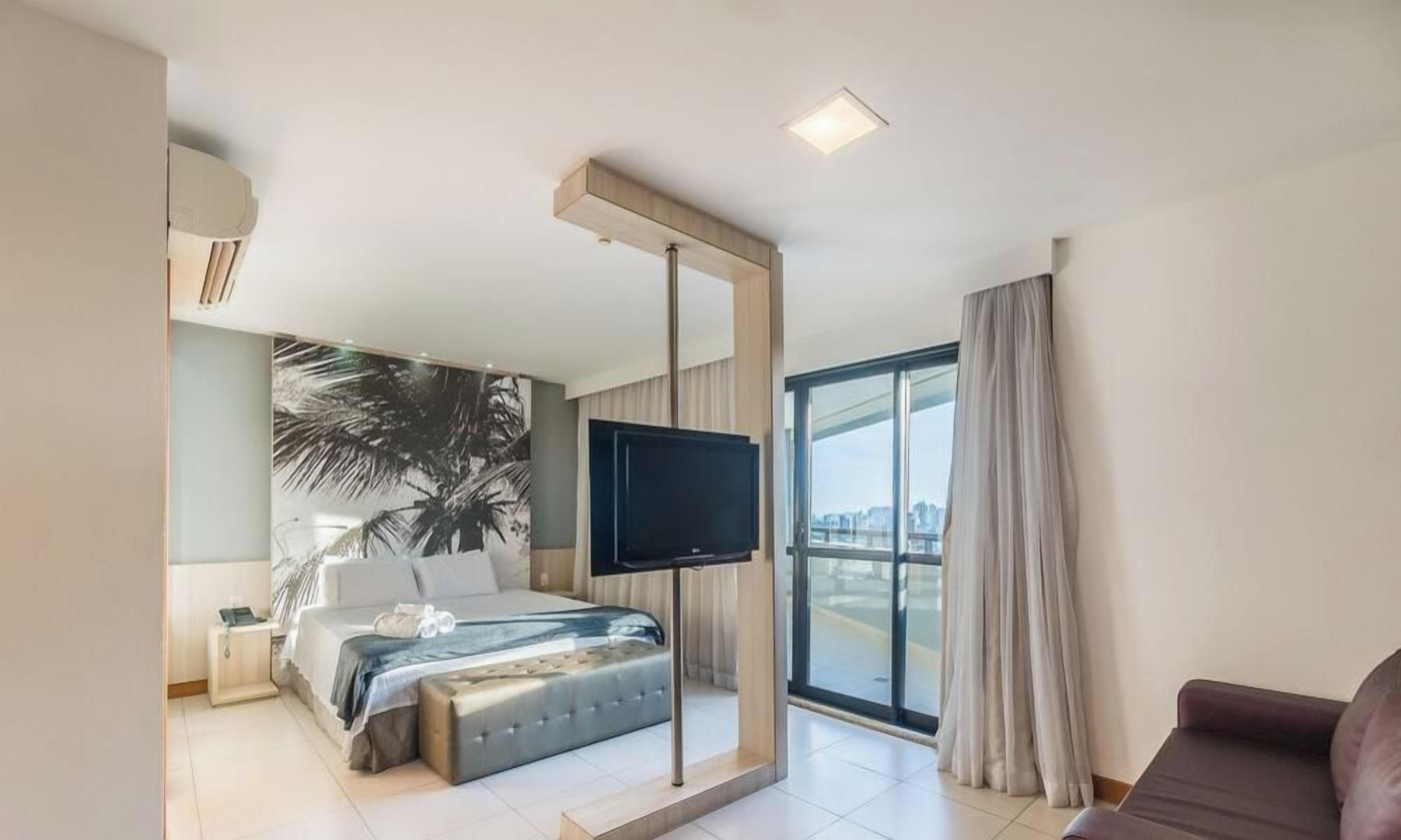 Une chambre d’hôtel moderne équipée d’un lit, d’un téléviseur à écran plat, d’une grande fenêtre et d’un balcon.