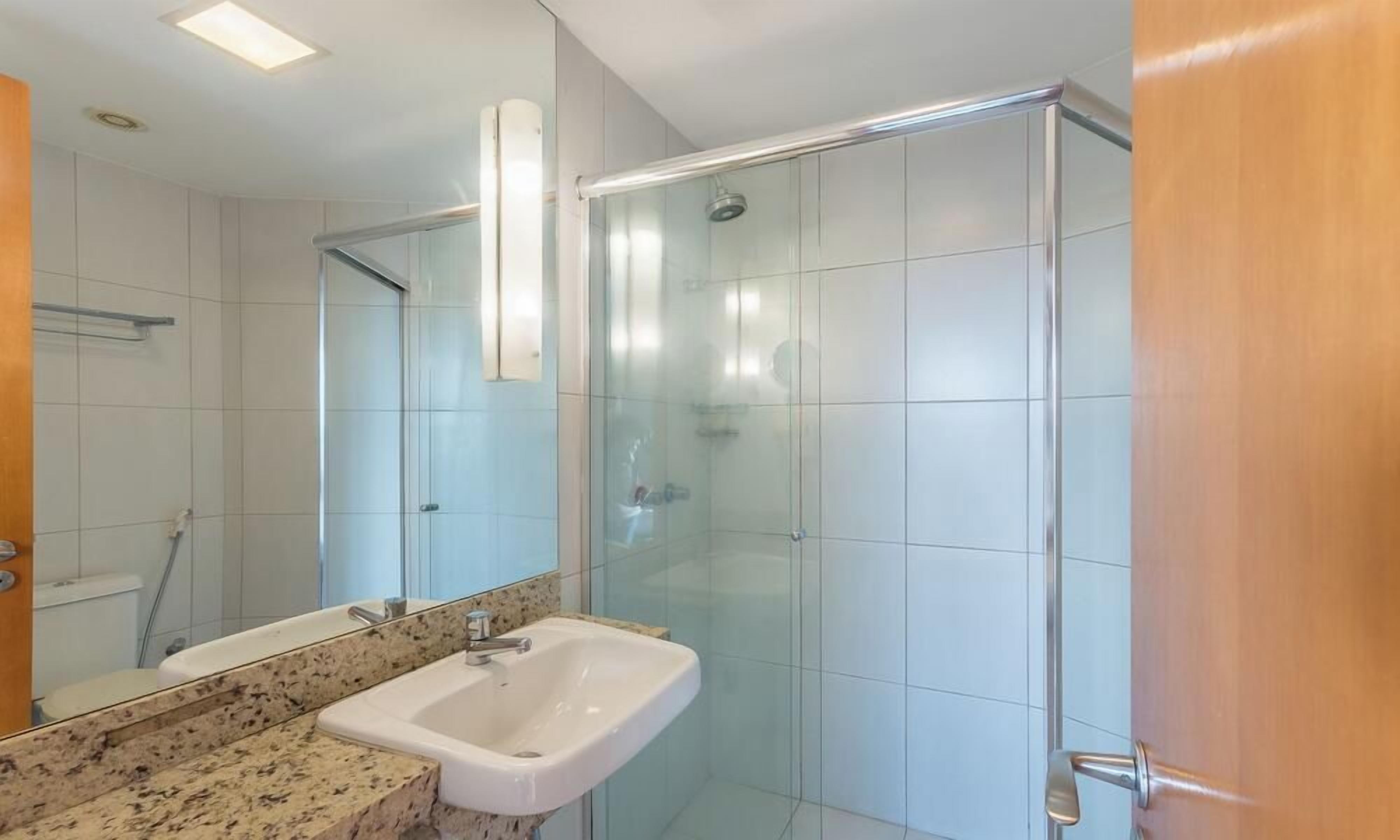 A bathroom with a glass shower enclosure, a sink with a granite countertop, and a mirror.