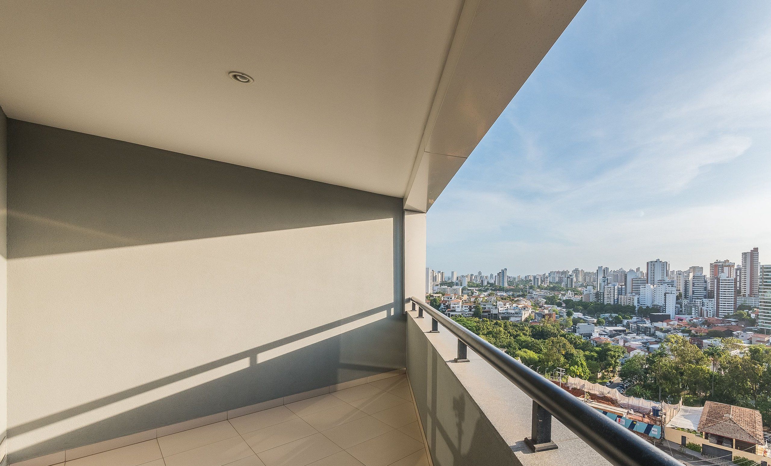A balcony with a city view, a tiled floor, and a metal railing.