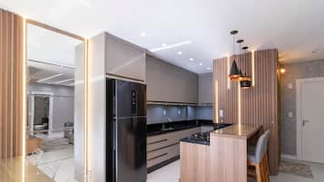 A modern kitchen with a black refrigerator, wooden bar counter, and recessed ceiling lighting.