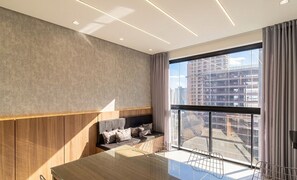Una habitación de hotel moderna con un ventanal grande, una pared de acento de madera, un sofá y una mesa de comedor.