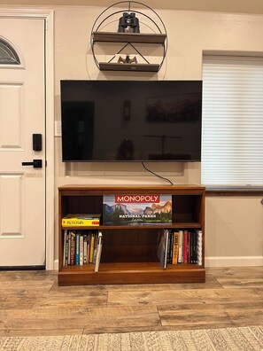 Een kamer met een aan de muur bevestigde televisie, een boekenkast met gezelschapsspellen en een deur met een raam.