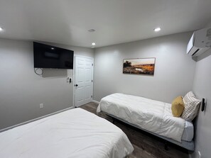 Een slaapkamer met twee bedden, een aan de muur bevestigde televisie en een airconditioning.