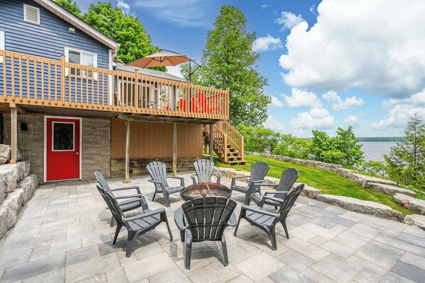 A deck with Adirondack chairs and a fire pit, overlooking a body of water.
