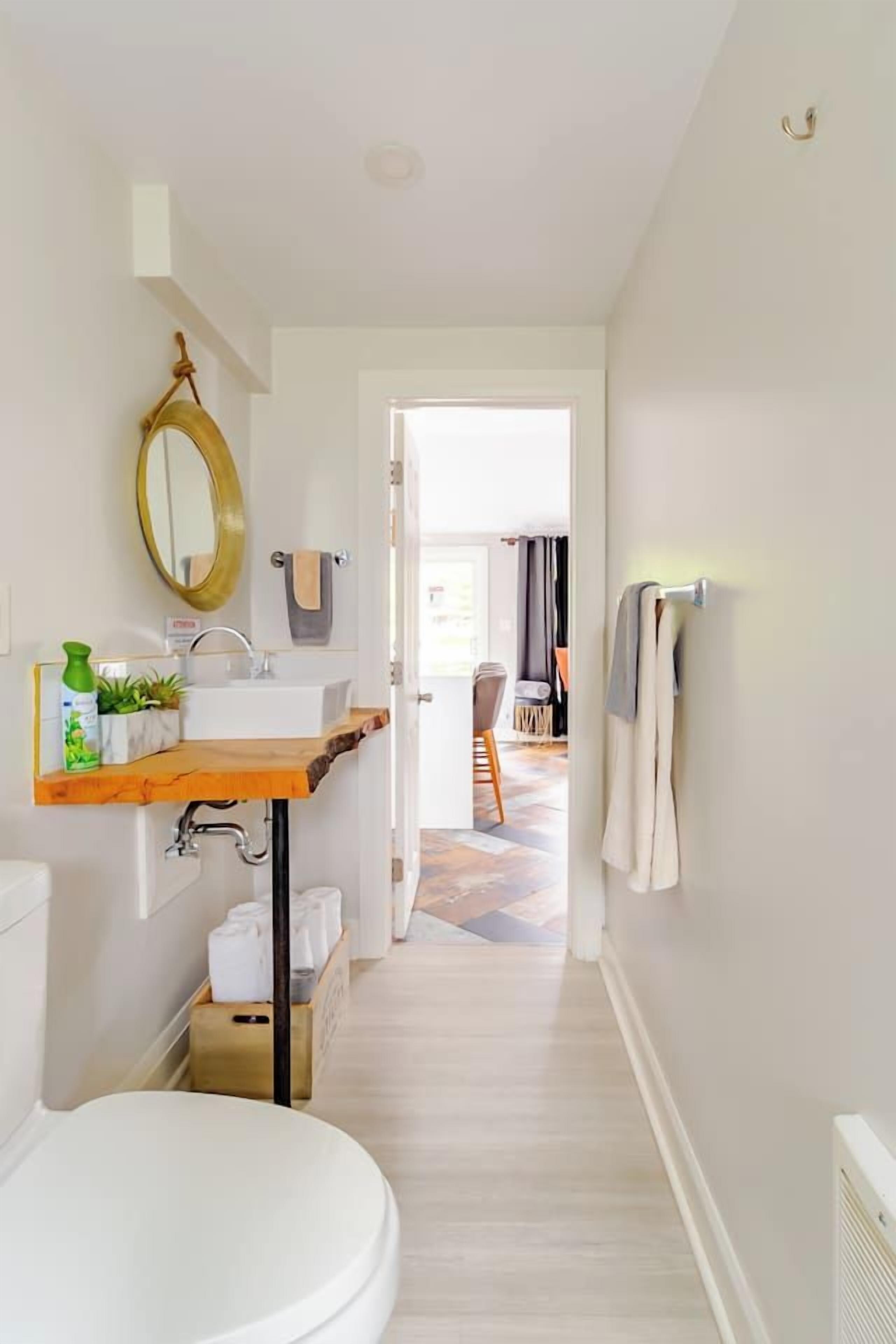 A narrow hallway leading to a bathroom with a toilet, sink, and mirror.