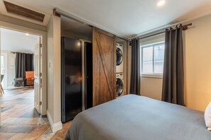 A hotel room with a bed, a washing machine, and a large window with curtains.