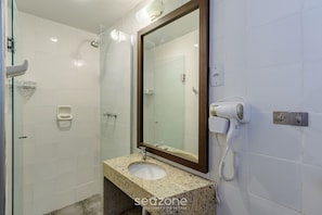 Ein Badezimmer mit Duschabtrennung aus Glas, einem Waschbecken mit Marmorplatte und einem an der Wand befestigten Föhn.
