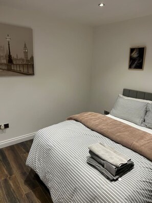 A bedroom with a bed, pillows, a blanket, a painting, and a nightstand.