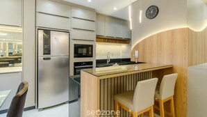 A modern kitchen with a built-in refrigerator, microwave, and stove. There is a glass island with seating and a clock on the wall. - Apt w/ Private BBQ 90m From the Sea Rih0802 (Porto Belo)