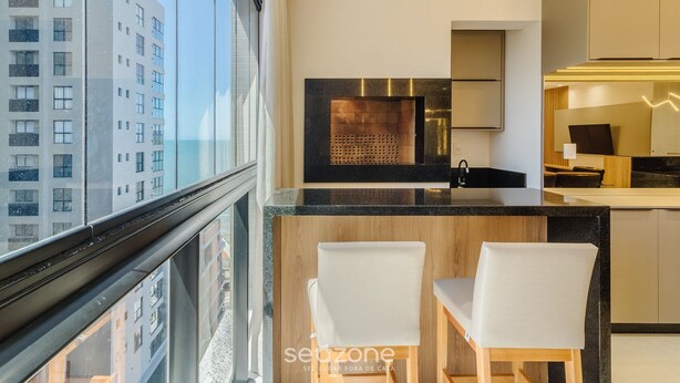 A modern kitchen with a large window, a built-in stove, and two white bar stools. - Apt w/ Private BBQ 90m From the Sea Rih0802 (Porto Belo)