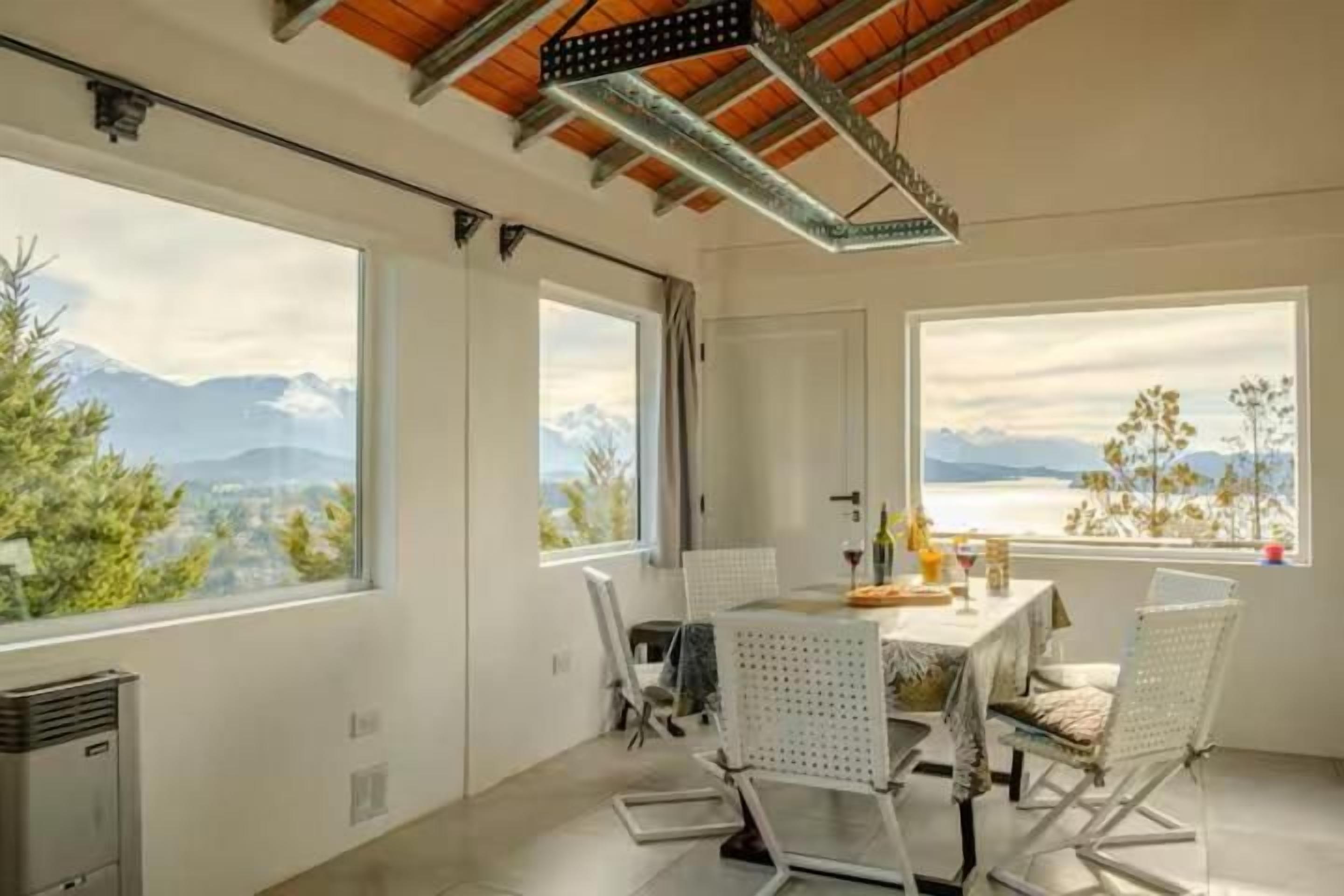 Comedor con mesa y sillas, ventanas amplias con vista a la montaña y techo con vigas a la vista.
