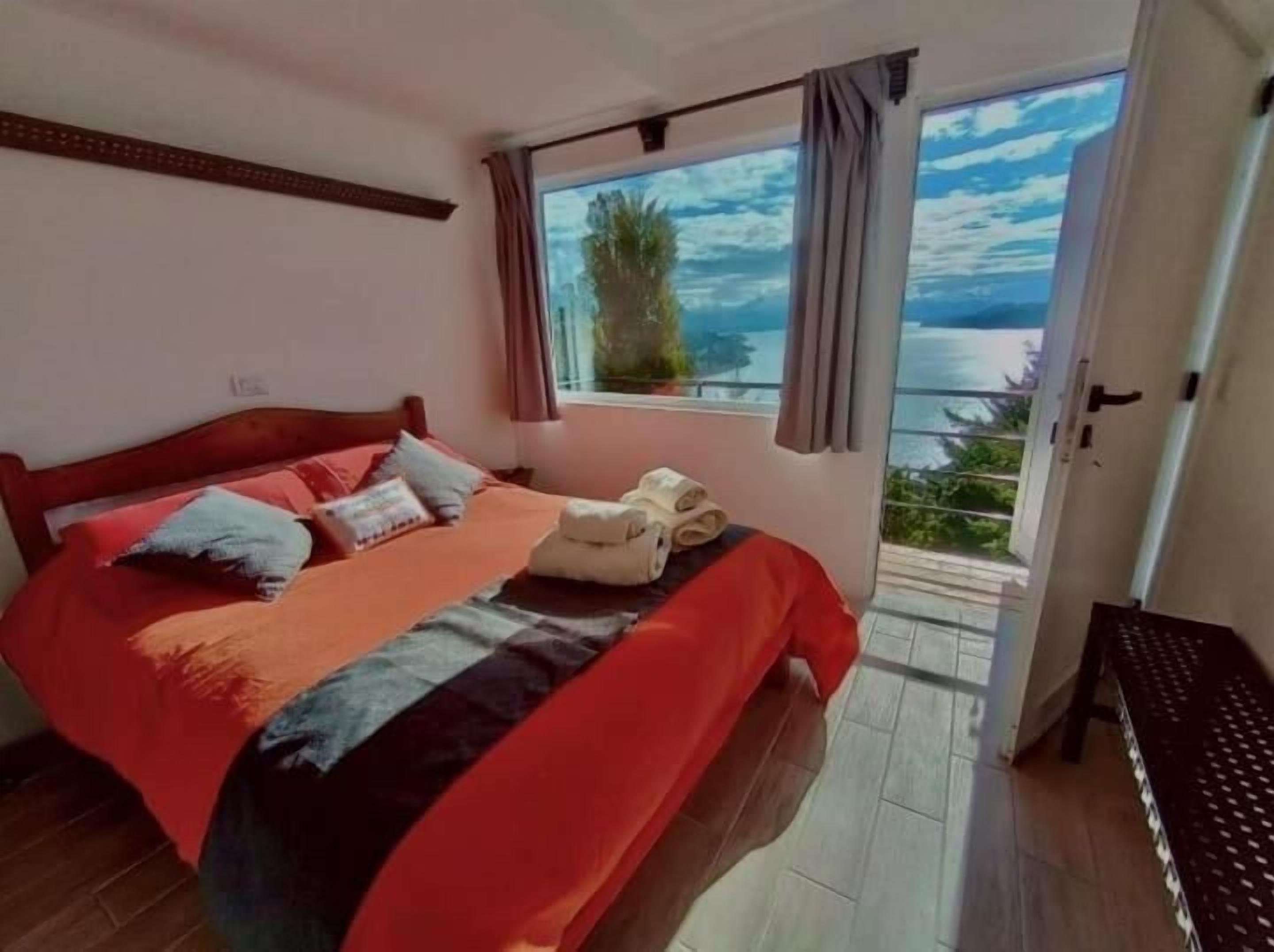 Un dormitorio con cama, ventana con vistas y puerta que da a un balcón.