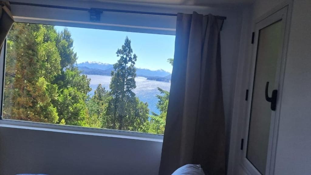 Habitación con ventana que da a un paisaje montañoso y un cuerpo de agua.