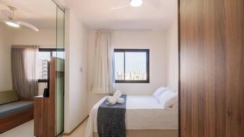 A hotel room with a bed, a seating area, a large window with a city view, and a ceiling fan.