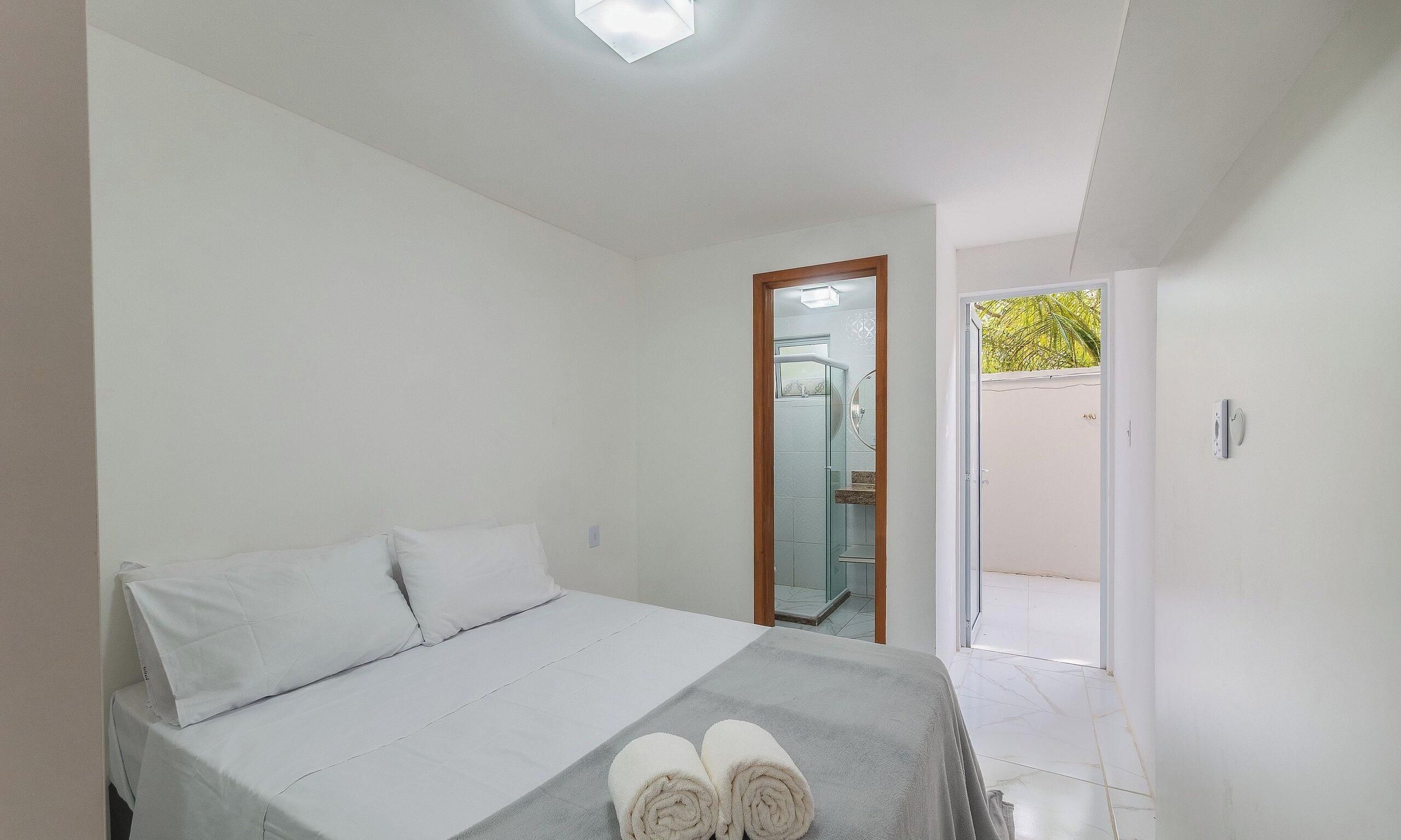 Ein Schlafzimmer mit einem Bett, Kissen, einem Handtuch und Blick auf ein Badezimmer und die Außenwelt.