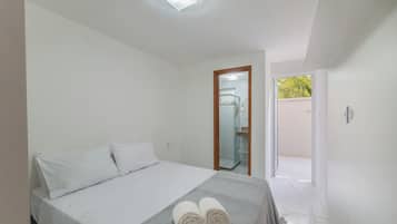 Quarto com cama, travesseiros, toalha e vista para um banheiro e o exterior.