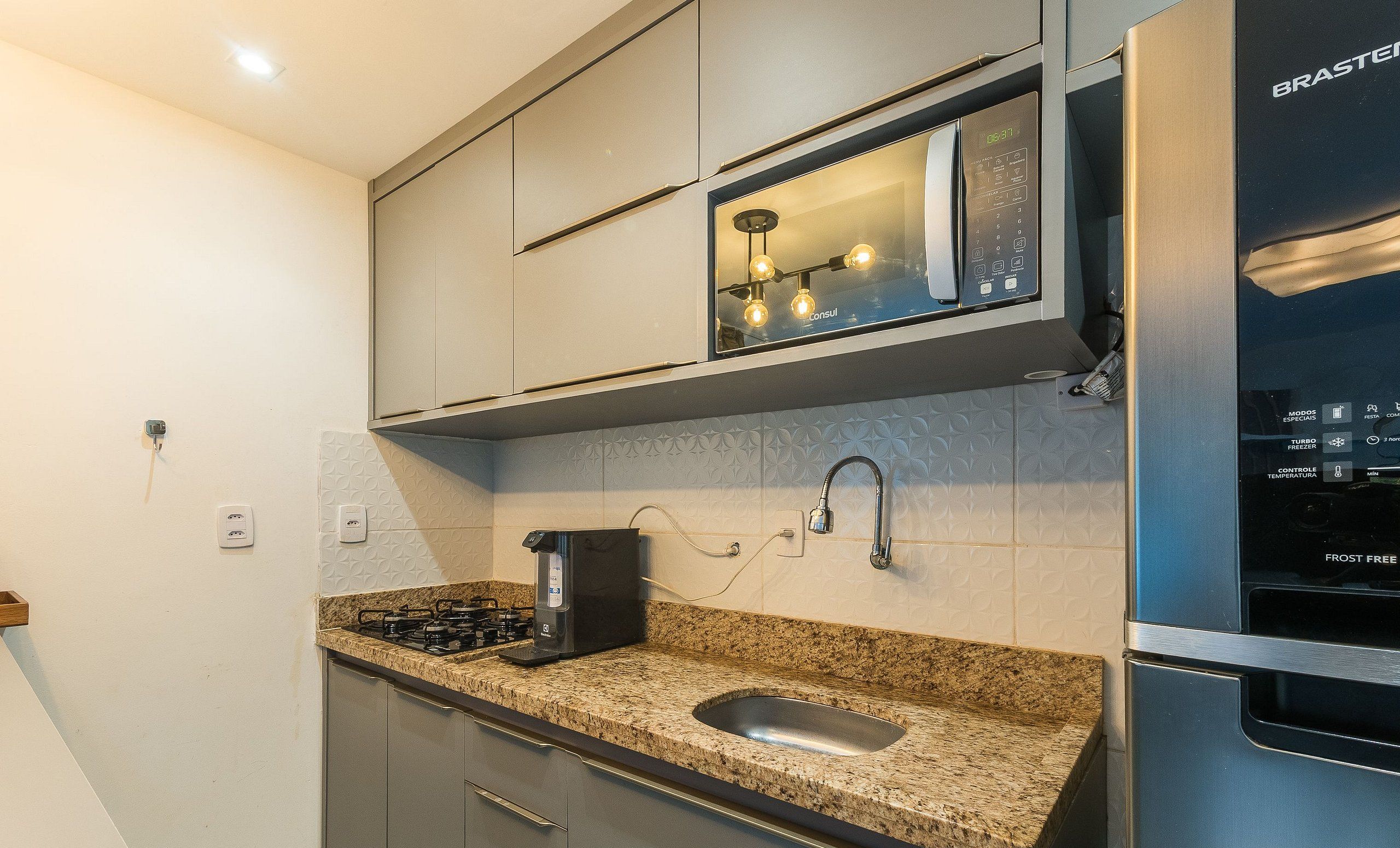 Uma cozinha moderna com micro-ondas embutido, geladeira de aço inoxidável e bancada de granito.
