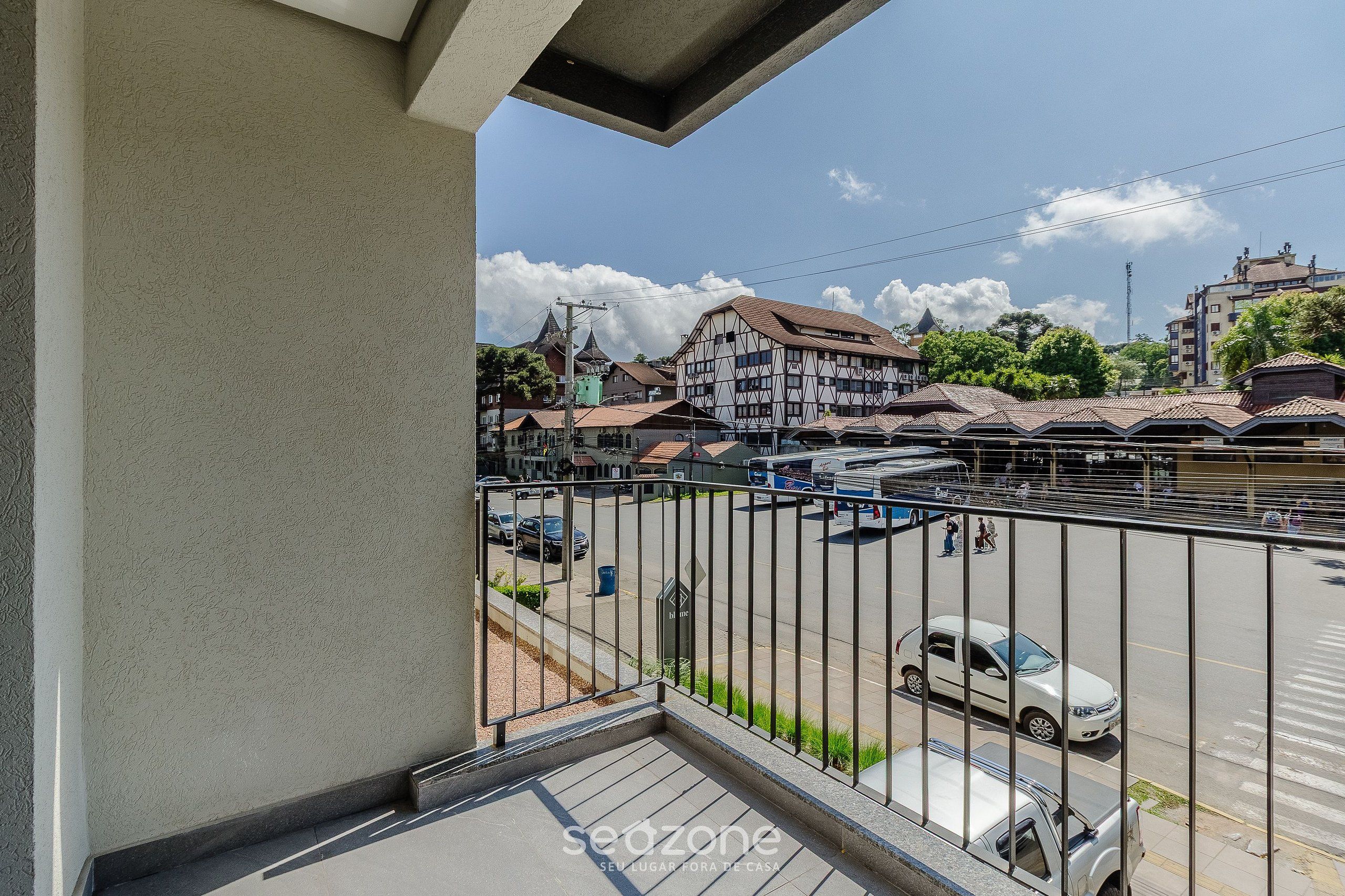 A balcony with a view of a street, buildings, and parked cars.