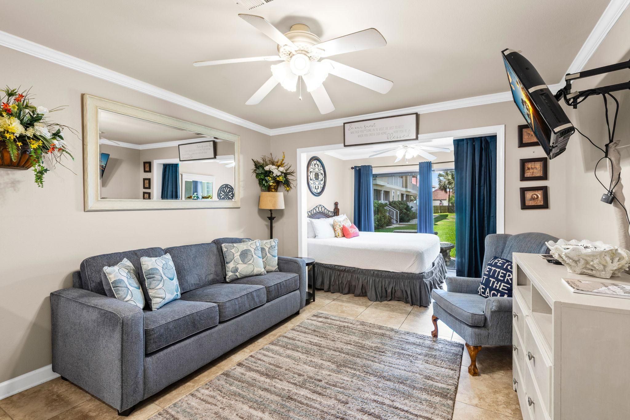 Een goed verlichte kamer met een plafondventilator, een bed met uitzicht, een bank, een stoel en een bureau met een lamp.