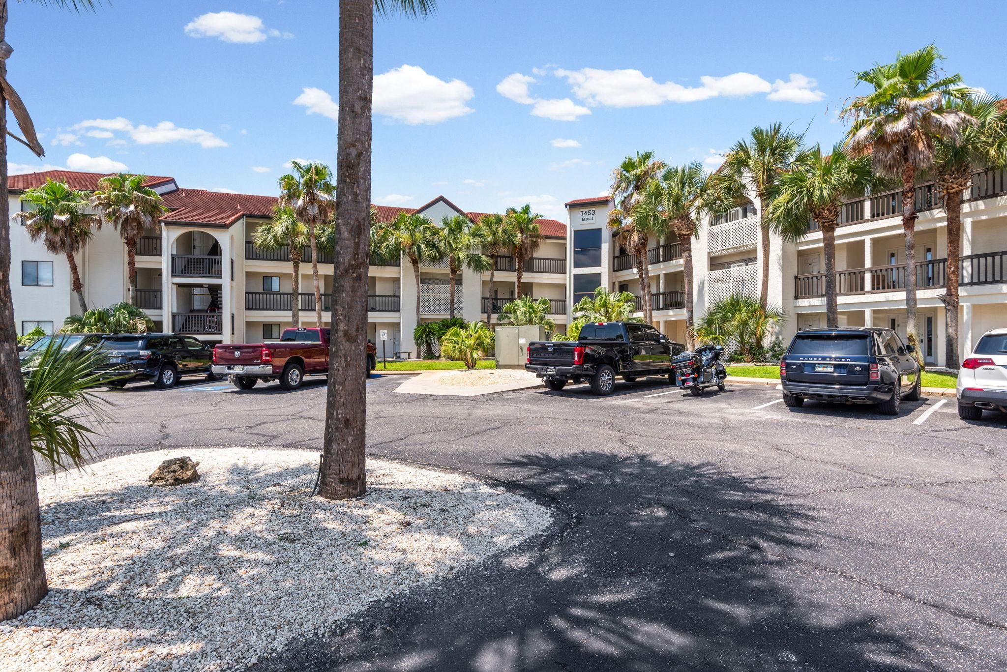 A multi-story hotel with a parking lot, palm trees, and a clear sky.
