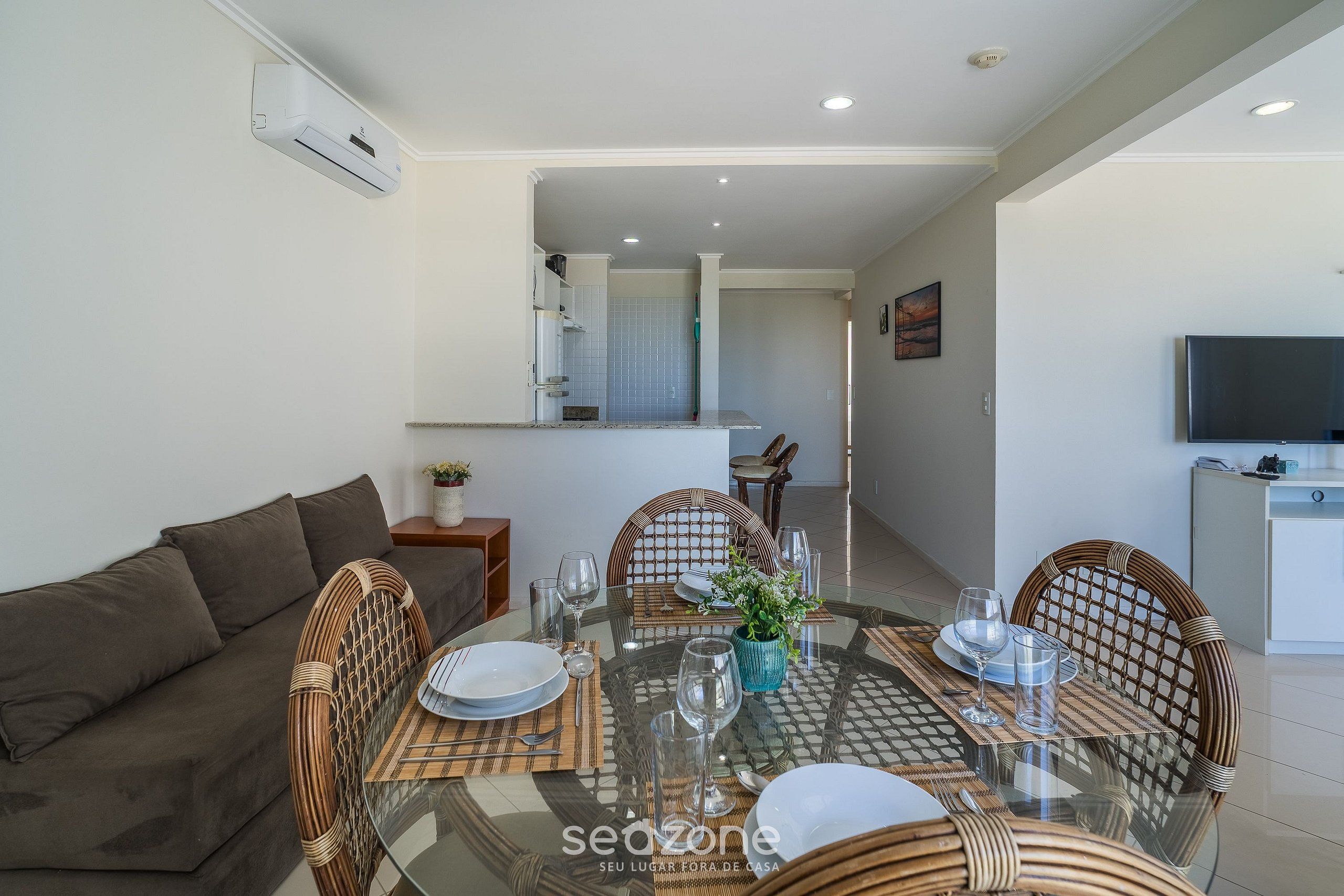 A modern dining area with a glass table, wicker chairs, and a white sofa.