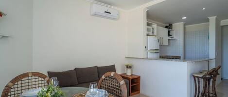 Un espacio habitable compacto con kitchenette, una zona de comedor con mesa y sillas, y un sofá.