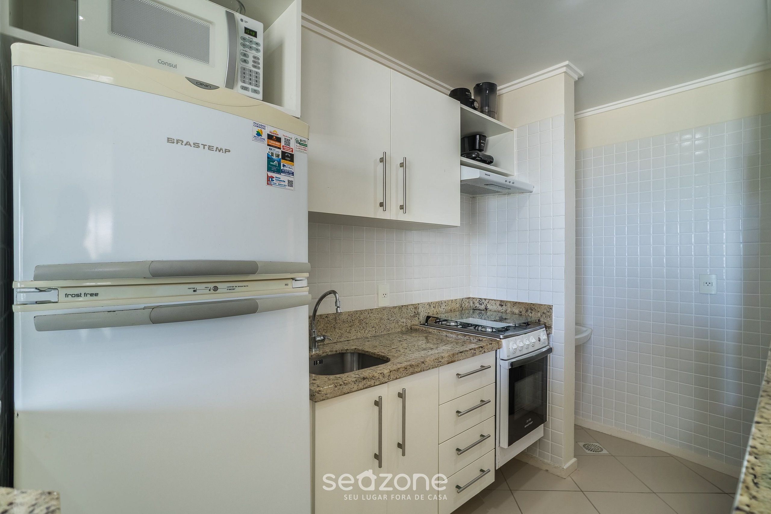 Una cocina con gabinetes blancos, un lavamanos de acero inoxidable, una estufa y un microondas.