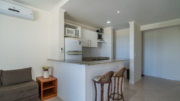 A compact kitchen with a built-in microwave, a refrigerator, and a gas stove. There are two wicker bar stools and a small wooden side table with a vase.