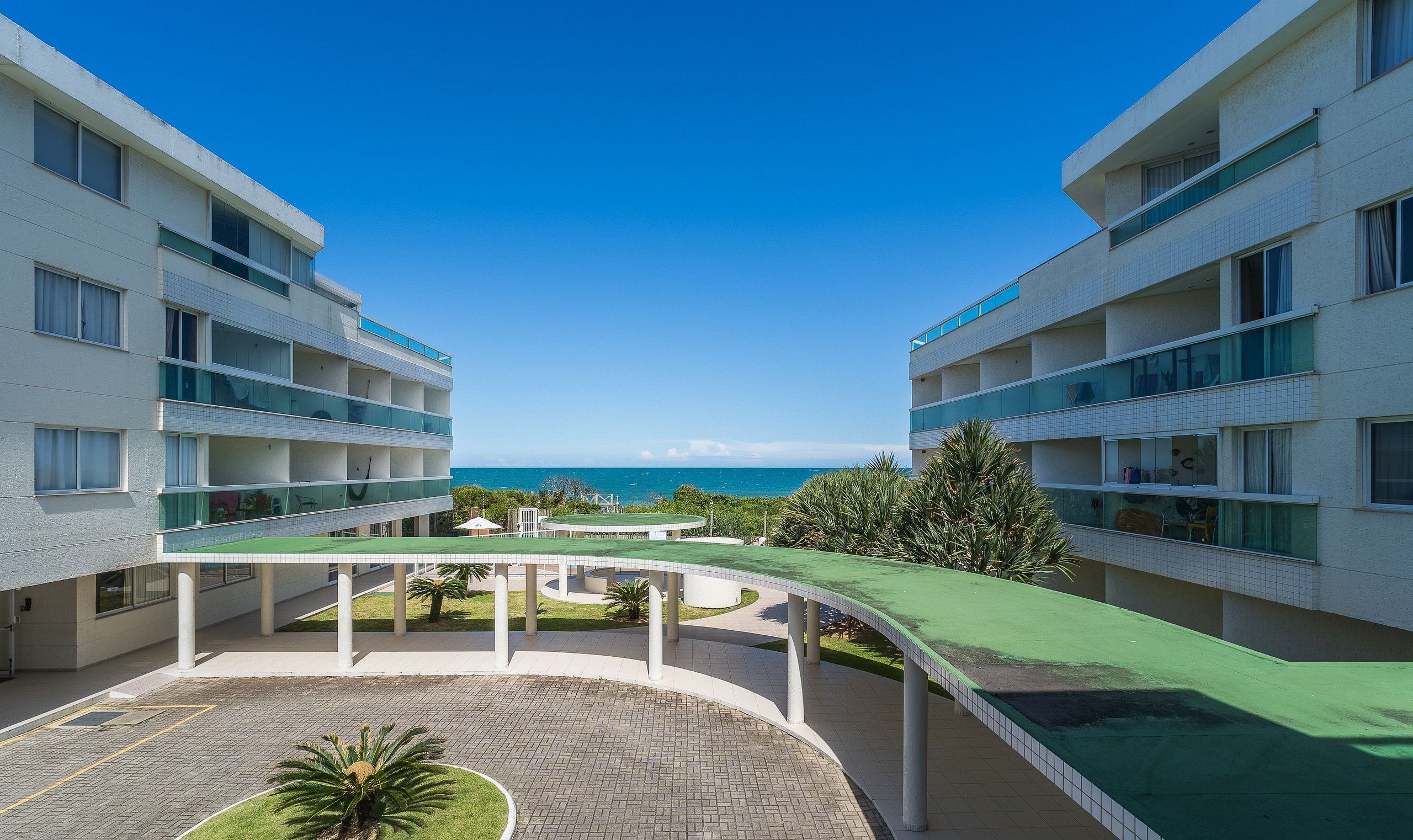 A modern hotel with a central courtyard, multiple balconies, and a view of the sea.