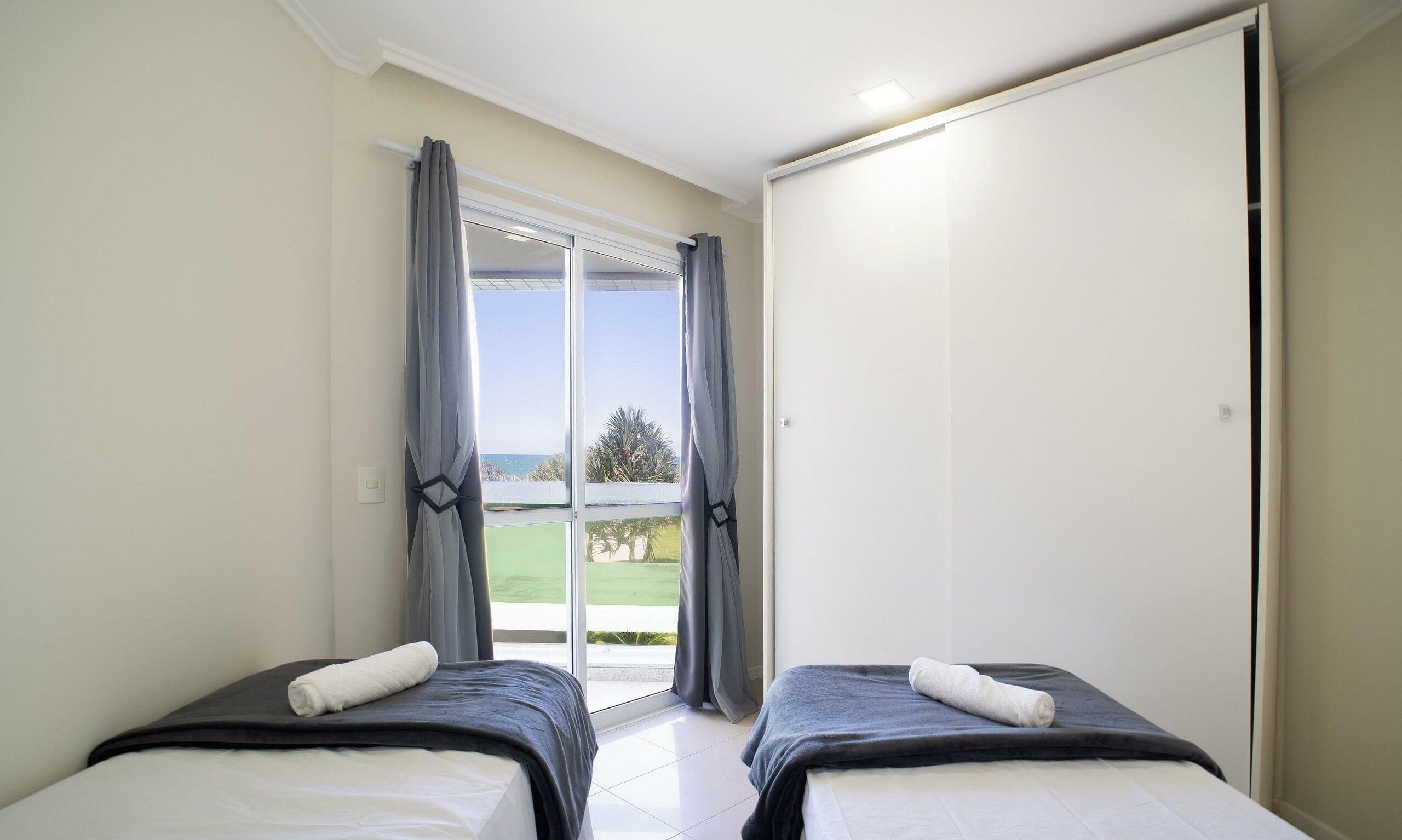 Un dormitorio con dos camas, puerta corrediza a un balcón y vistas al exterior.