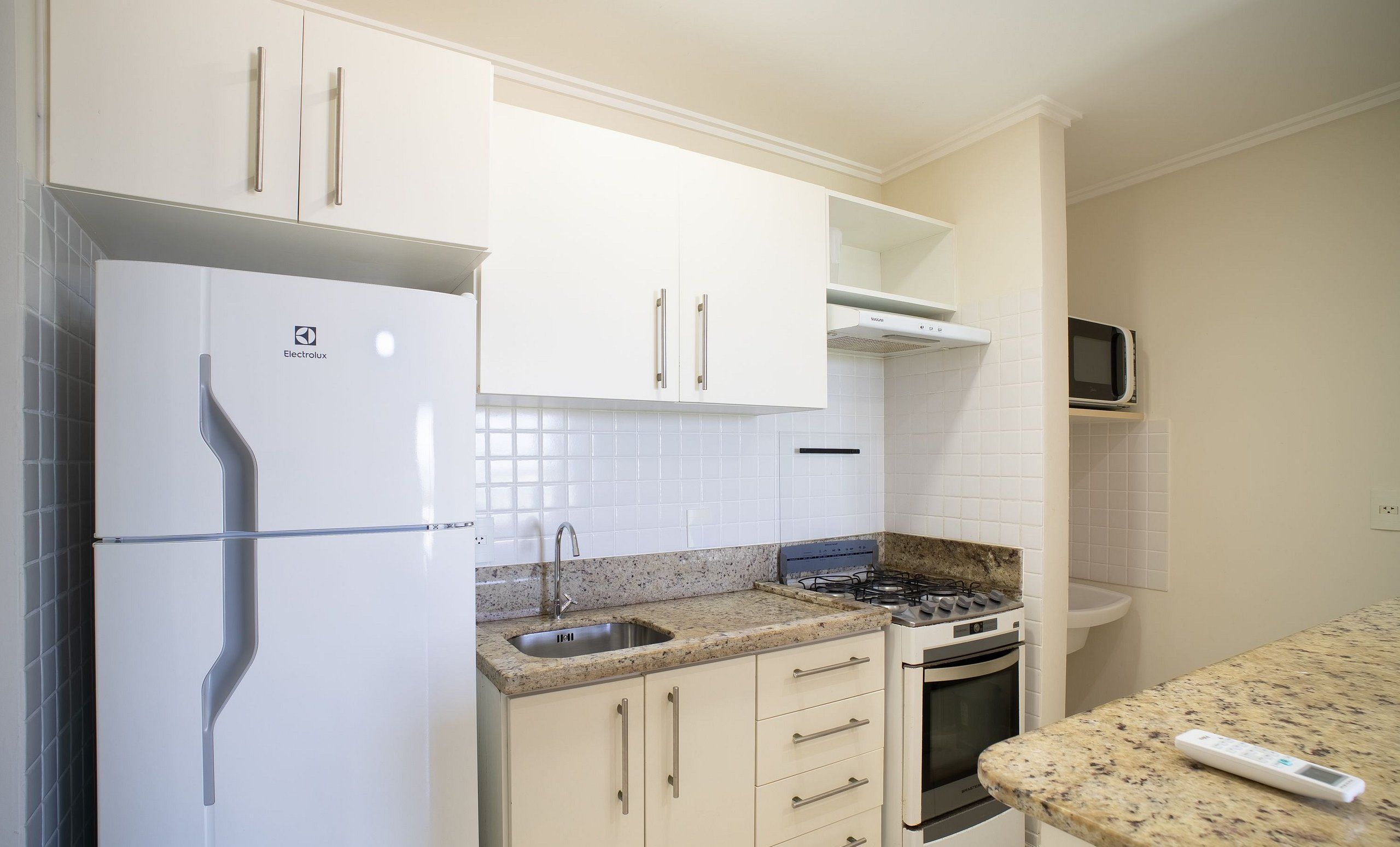 Una cocina con armarios blancos, un refrigerador de acero inoxidable, un microondas, una estufa a gas y un lavamanos.
