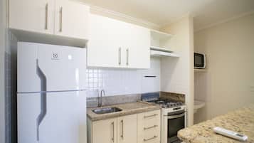 Una cocina con armarios blancos, un refrigerador de acero inoxidable, un microondas, una estufa a gas y un lavamanos.