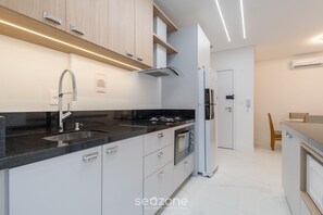A modern kitchen with a black countertop, stainless steel appliances, and white cabinetry. - Apt w/ Barbecue Grill 500 m From the Beach Stw1206 (Itapema)